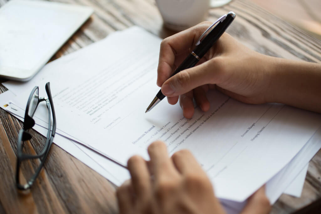 A man with ballpoint pen filling insurance papers. Close-up of male hands working at desk. Analyzing documents concept