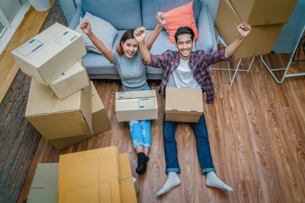 Top view Asian young couple are glad after successfull packing the cardboard box for moving in new house, Helping relocate and joshing together, Moving and House Hunting concept, selective focus