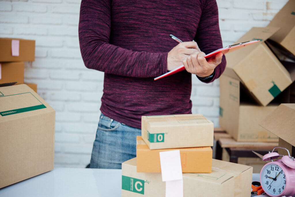 Handsome Young man working with papers among parcels at table in delivery department. online concept