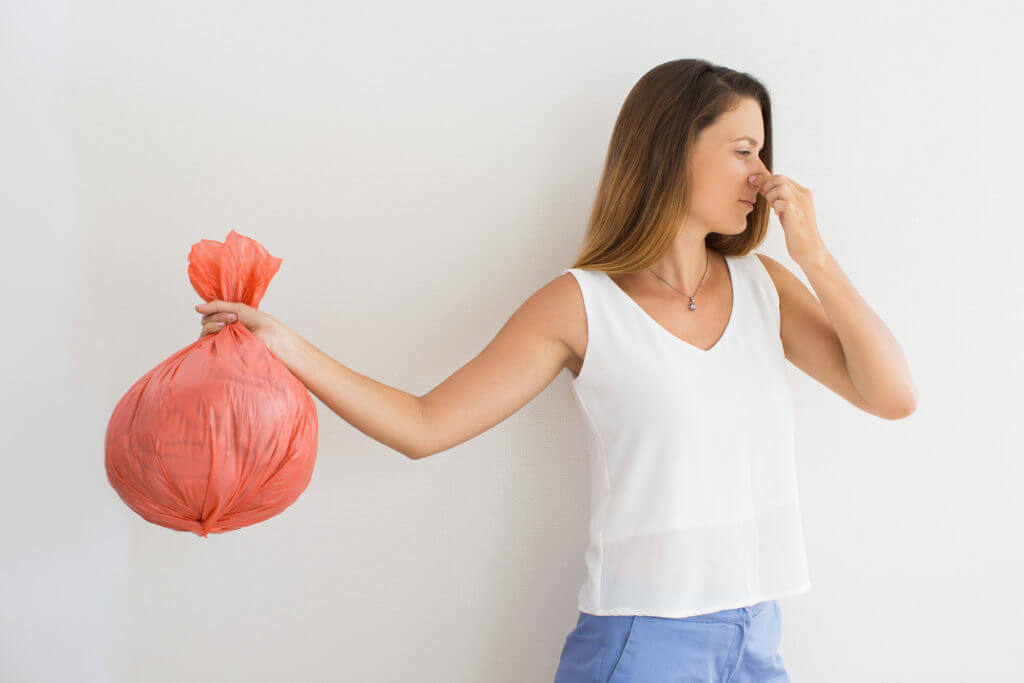 Displeased young woman with pinched face holding garbage bag and holding her nose. Unpleasant smell concept